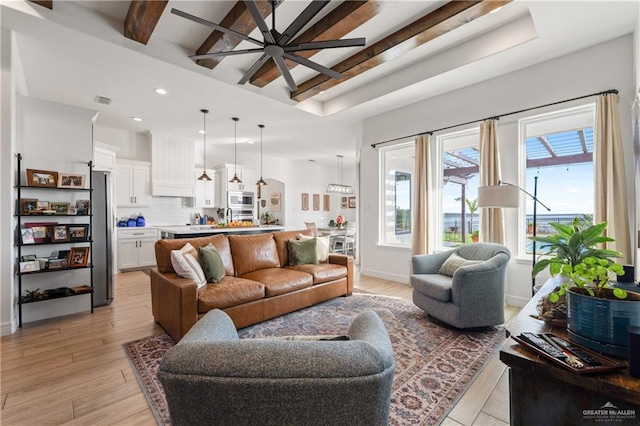 living room with beam ceiling, a wealth of natural light, ceiling fan, and light wood-type flooring