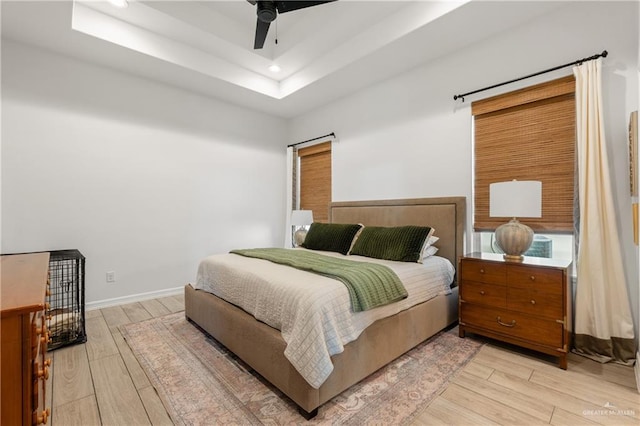 bedroom with a tray ceiling, ceiling fan, and light hardwood / wood-style floors