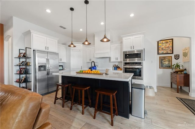 kitchen featuring stainless steel appliances, backsplash, an island with sink, pendant lighting, and white cabinets