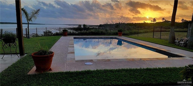 pool at dusk featuring a lawn, a water view, and a patio