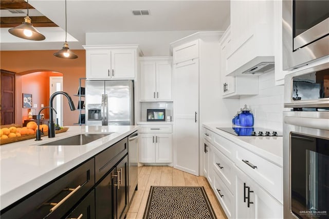 kitchen featuring appliances with stainless steel finishes, sink, pendant lighting, white cabinets, and light hardwood / wood-style floors