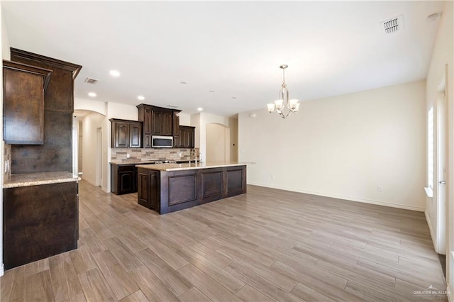 7303 Umar Ave, Mission, TX 78573 - kitchen featuring stainless steel microwave, arched walkways, a chandelier, dark brown cabinetry, and tasteful backsplash