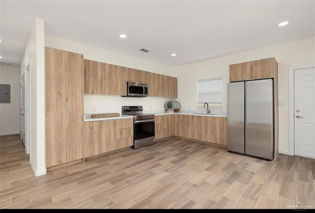 kitchen with electric panel, sink, light wood-type flooring, light brown cabinetry, and appliances with stainless steel finishes