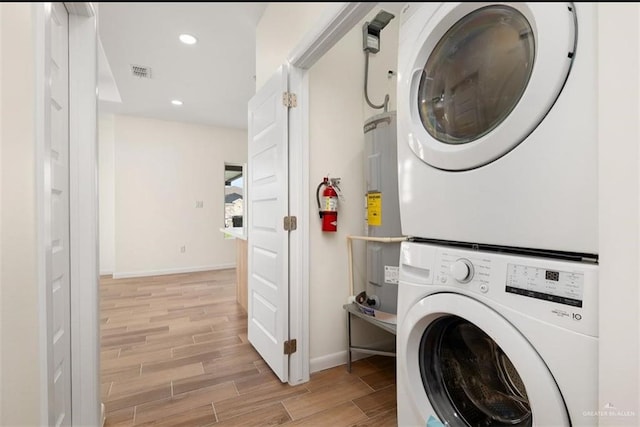 laundry room with stacked washer / drying machine, light hardwood / wood-style floors, and electric water heater