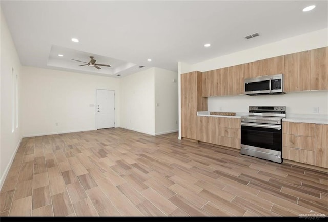 kitchen with a raised ceiling, ceiling fan, light wood-type flooring, light brown cabinetry, and stainless steel appliances