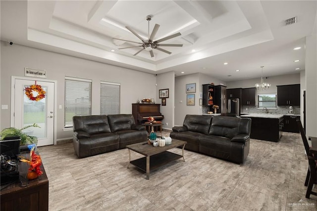 living room featuring ceiling fan with notable chandelier, a raised ceiling, a healthy amount of sunlight, and sink