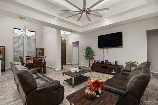 living room with ceiling fan with notable chandelier, a towering ceiling, and a raised ceiling