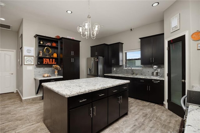 kitchen with stainless steel fridge, backsplash, a kitchen island, and sink