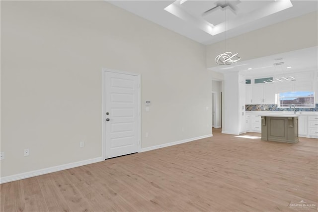 unfurnished living room featuring sink, ceiling fan, light wood-type flooring, a towering ceiling, and a tray ceiling