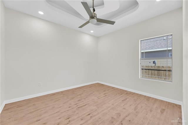 empty room with light wood-type flooring, a tray ceiling, and ceiling fan