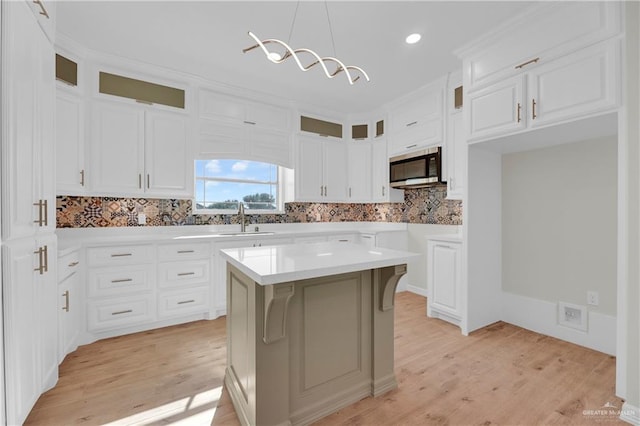 kitchen with white cabinets, sink, hanging light fixtures, light hardwood / wood-style flooring, and a kitchen island