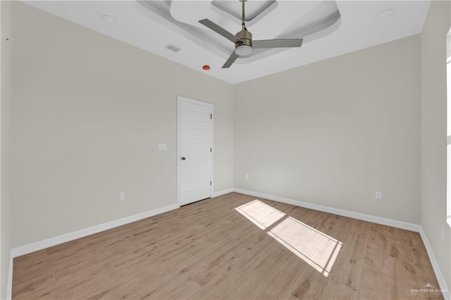 empty room featuring light hardwood / wood-style flooring, a raised ceiling, and ceiling fan