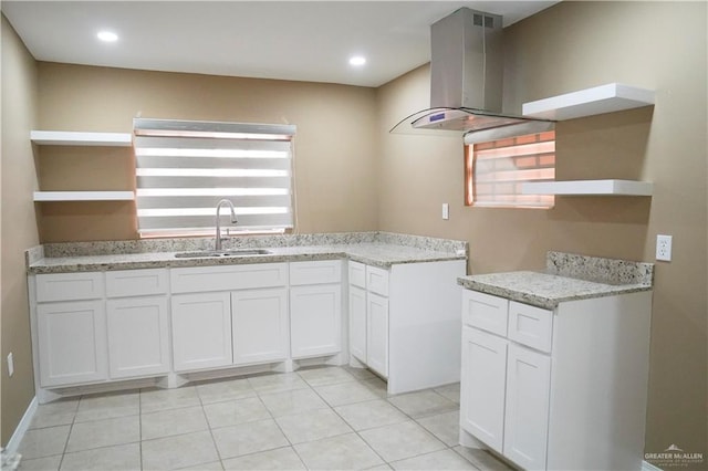 kitchen with light stone countertops, island range hood, white cabinetry, and sink