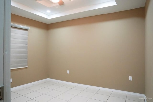 tiled spare room featuring ceiling fan and a tray ceiling