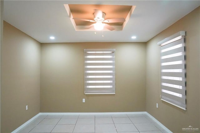 tiled spare room featuring a raised ceiling and ceiling fan