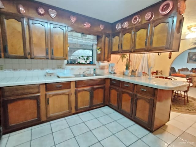 kitchen featuring backsplash, light tile patterned flooring, kitchen peninsula, and sink