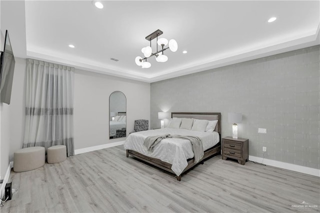 bedroom featuring a chandelier, a raised ceiling, baseboards, and wood finished floors