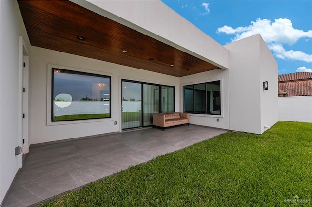 back of property featuring a lawn, a patio area, and stucco siding