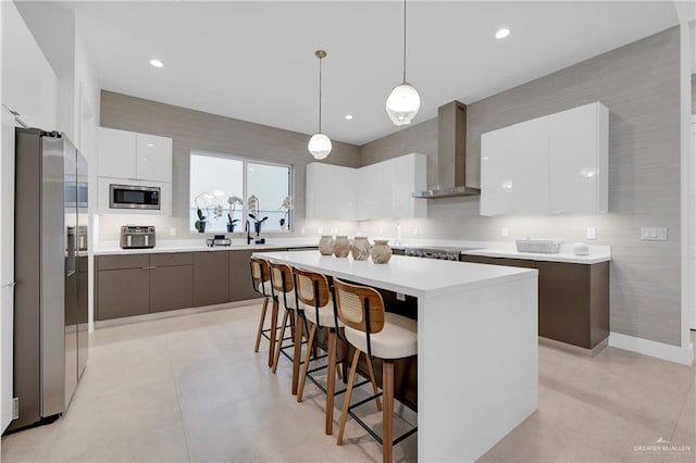 kitchen featuring a center island, a breakfast bar area, stainless steel appliances, modern cabinets, and wall chimney exhaust hood