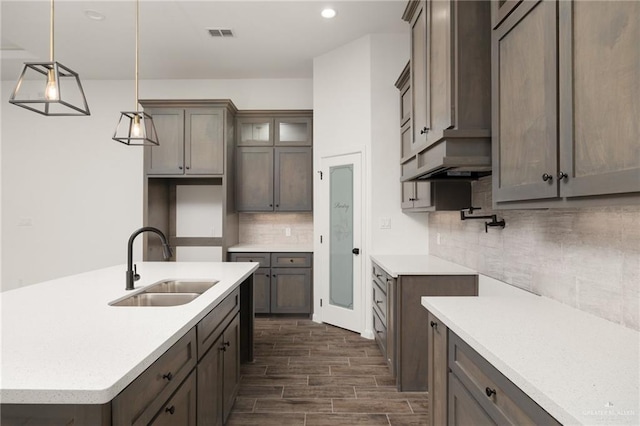 kitchen featuring sink, hanging light fixtures, dark hardwood / wood-style flooring, backsplash, and an island with sink