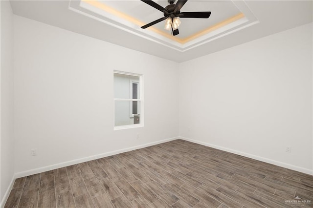 spare room with a raised ceiling, ceiling fan, and wood-type flooring