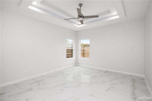 spare room with baseboards, a raised ceiling, ceiling fan, and marble finish floor
