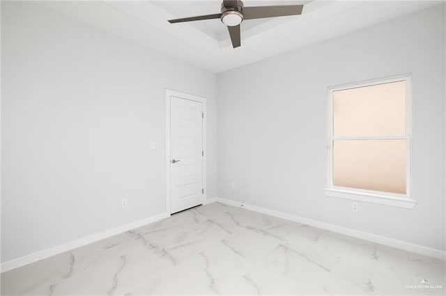unfurnished room featuring a ceiling fan, a raised ceiling, marble finish floor, and baseboards