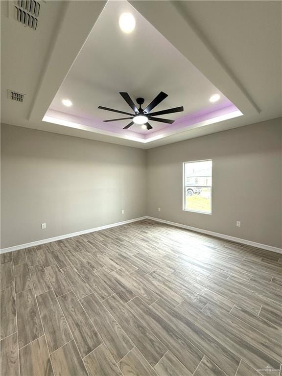 unfurnished room featuring ceiling fan, light hardwood / wood-style floors, and a tray ceiling