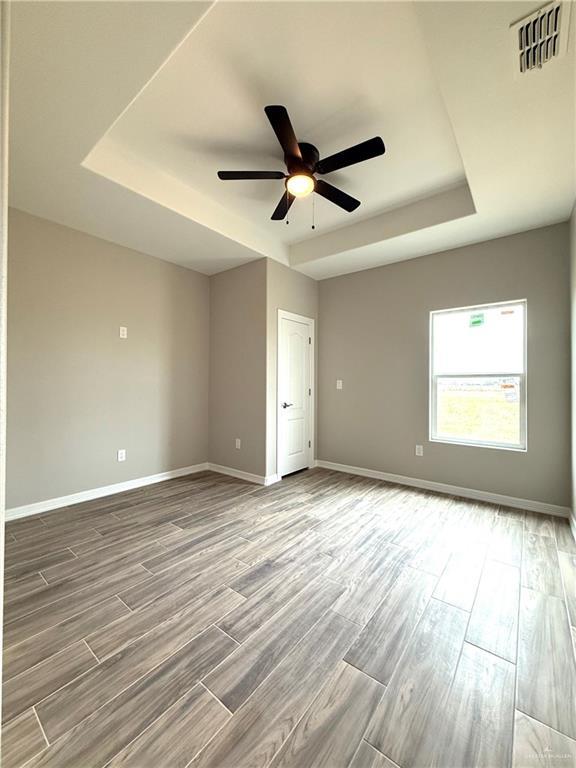 unfurnished room with a raised ceiling, hardwood / wood-style floors, and ceiling fan