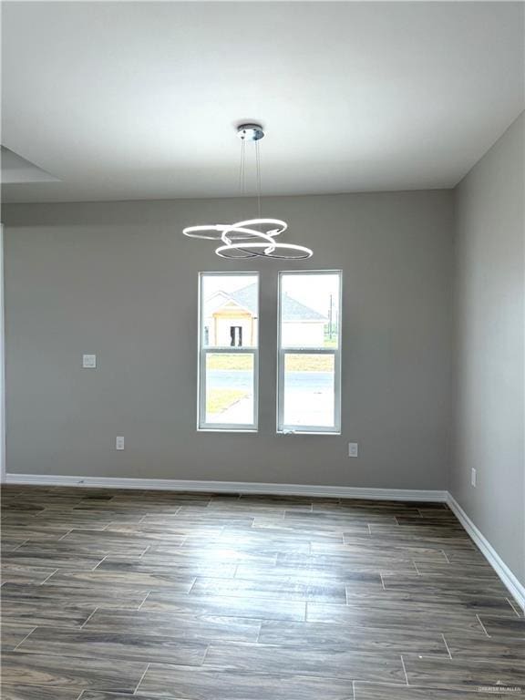 empty room with a notable chandelier and dark hardwood / wood-style flooring