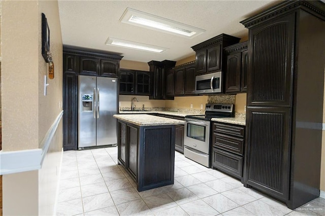 kitchen with stainless steel appliances, a center island, sink, and light stone counters