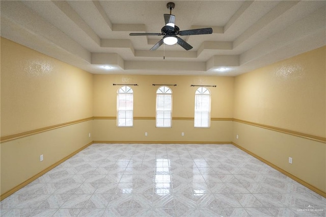 empty room with ceiling fan, plenty of natural light, and a tray ceiling