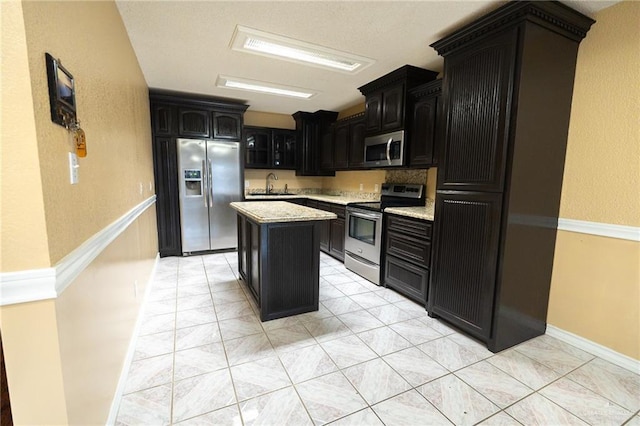 kitchen featuring sink, light tile patterned floors, stainless steel appliances, light stone counters, and a kitchen island