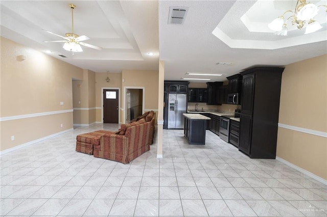 kitchen with sink, appliances with stainless steel finishes, a center island, a tray ceiling, and ceiling fan with notable chandelier