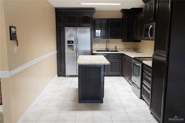 kitchen featuring stainless steel appliances, light stone countertops, a kitchen island, and sink