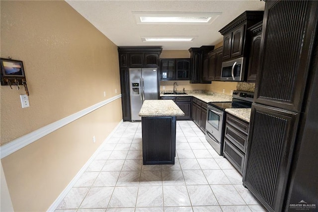 kitchen featuring light tile patterned floors, sink, appliances with stainless steel finishes, a center island, and light stone counters