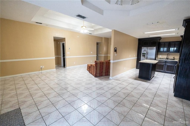 kitchen featuring ceiling fan, stainless steel refrigerator with ice dispenser, a kitchen island, light tile patterned flooring, and a raised ceiling