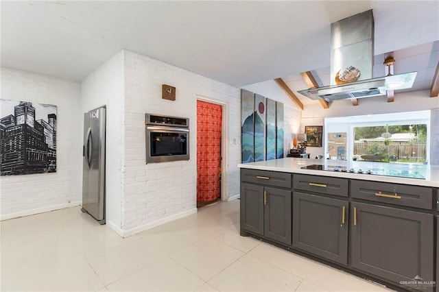 kitchen featuring brick wall, stainless steel appliances, island range hood, light tile patterned floors, and lofted ceiling