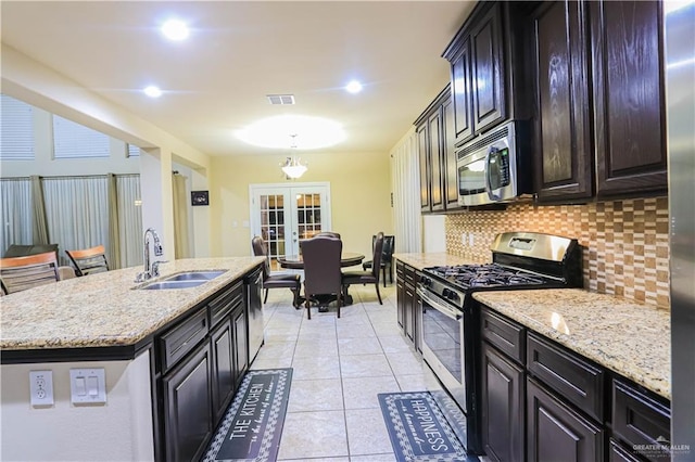 kitchen with sink, french doors, stainless steel appliances, tasteful backsplash, and a kitchen island with sink