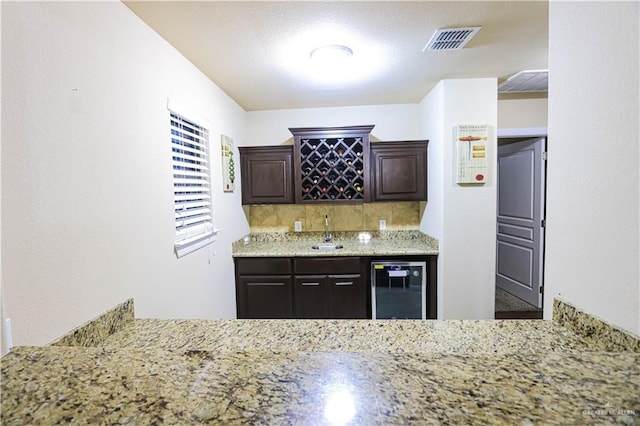 kitchen featuring light stone countertops, dark brown cabinetry, sink, and wine cooler