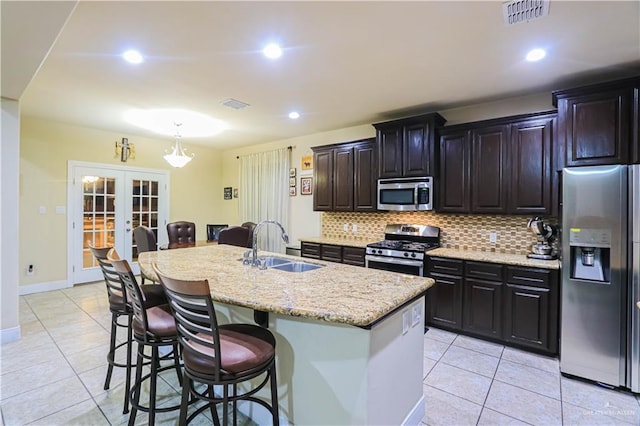 kitchen featuring french doors, sink, stainless steel appliances, a breakfast bar area, and a kitchen island with sink