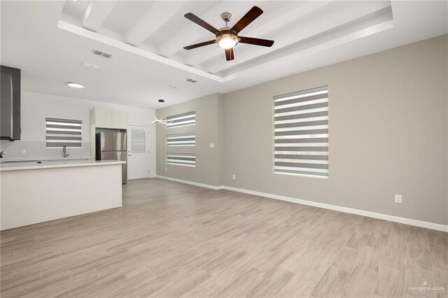 unfurnished living room featuring light hardwood / wood-style floors, a raised ceiling, and ceiling fan