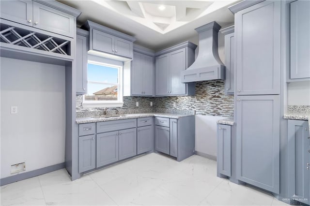 kitchen featuring premium range hood, gray cabinetry, light stone counters, and sink