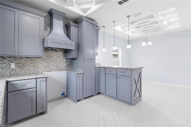 kitchen featuring backsplash, premium range hood, gray cabinetry, a raised ceiling, and decorative light fixtures