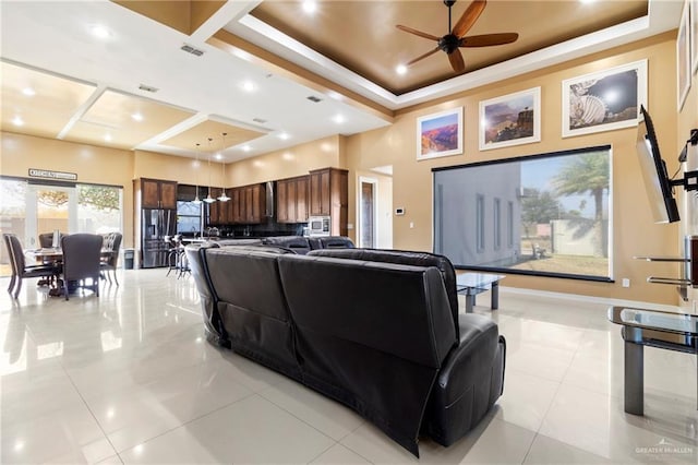 living room featuring a raised ceiling, a high ceiling, light tile patterned floors, and ceiling fan