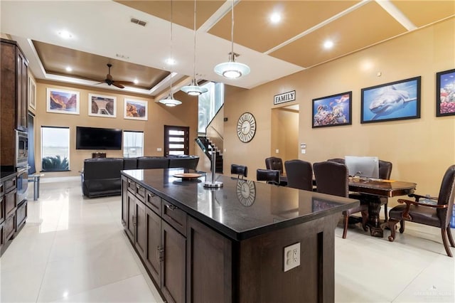 kitchen with decorative light fixtures, a center island, ceiling fan, dark brown cabinetry, and a raised ceiling