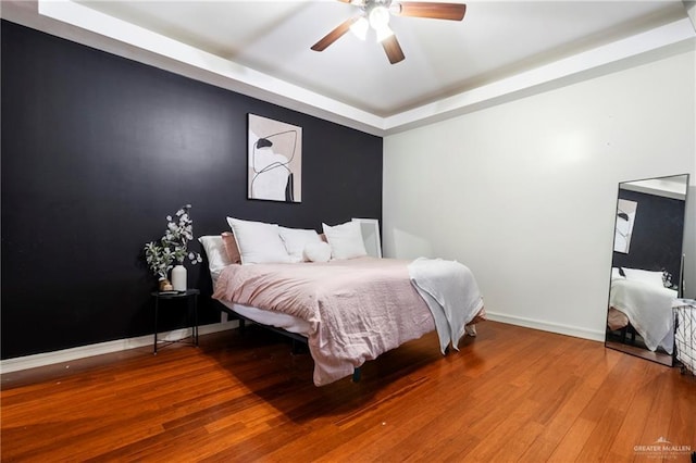 bedroom with wood-type flooring, ceiling fan, and a tray ceiling