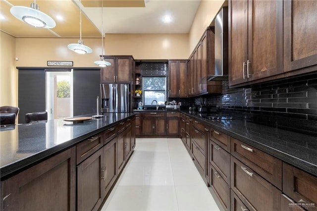 kitchen with stainless steel fridge, dark brown cabinets, tasteful backsplash, decorative light fixtures, and wall chimney exhaust hood