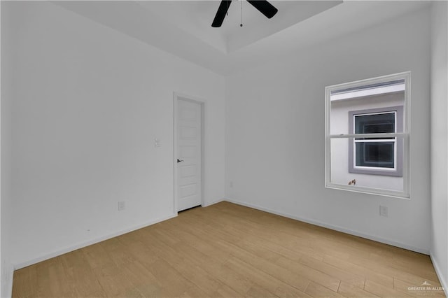 unfurnished room with ceiling fan, a tray ceiling, light wood finished floors, and baseboards