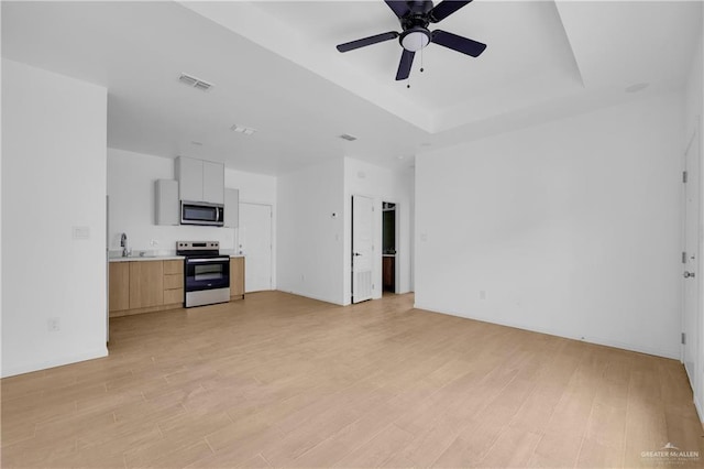 unfurnished living room featuring light wood-style flooring, visible vents, ceiling fan, and a tray ceiling